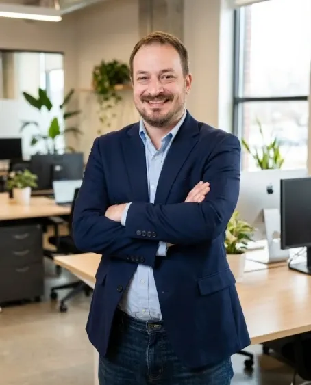 Alex Lamy in a navy blazer, arms crossed, in an office